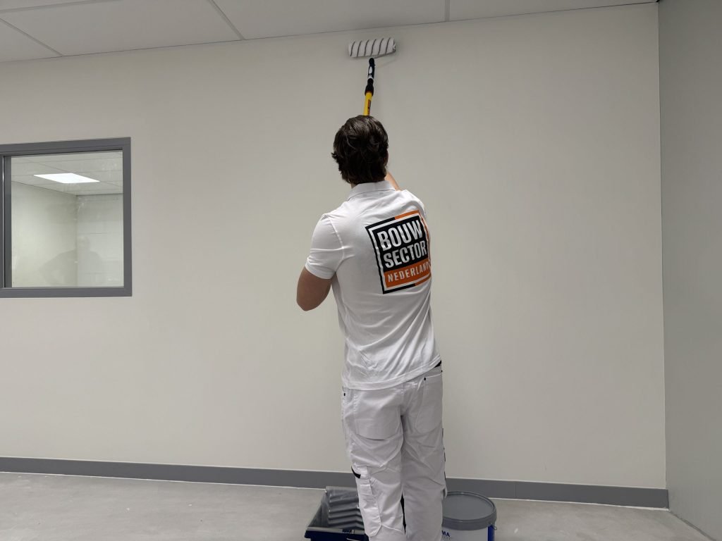 Schilder rolt de bovenrand van een witte muur bij het plafond in een nieuwe, lege ruimte