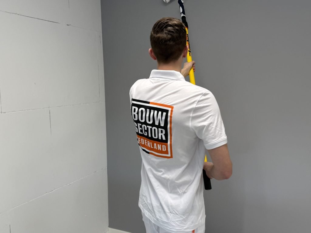 Schilder met roller op een lange steel werkt een grijze muur af tot aan het plafond
