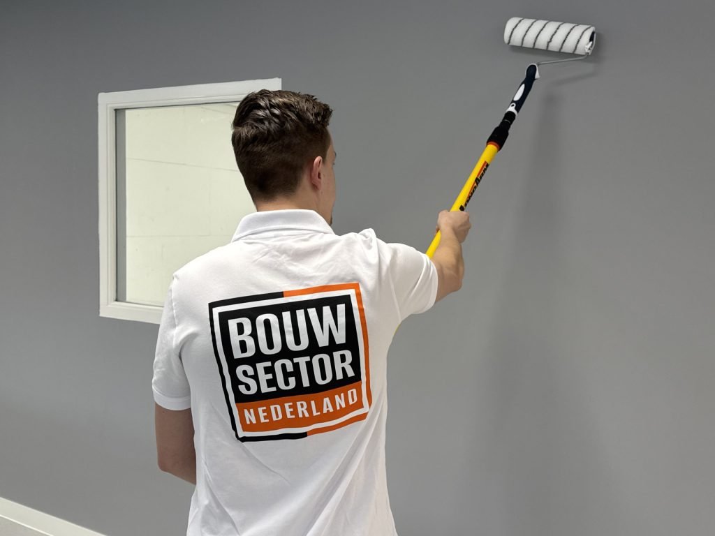 Vakman van Bouwsector Nederland zet een grijze wand in de verf met een roller op verlengsteel