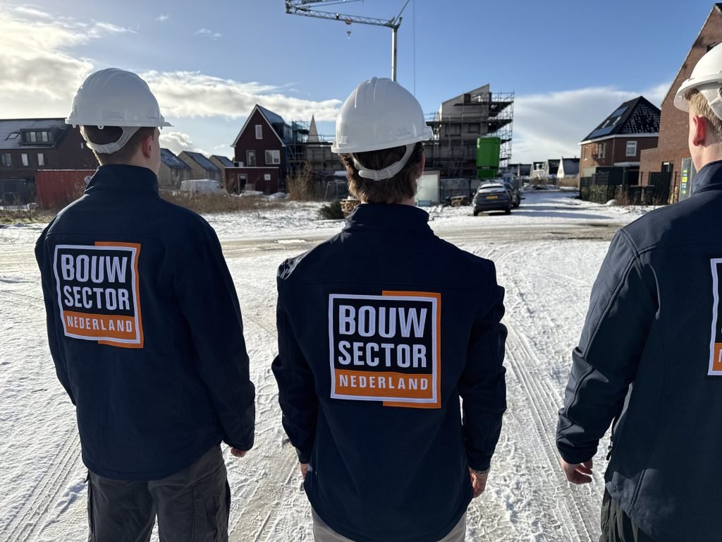 Drie vakmensen van Bouwsector Nederland met witte helm in een besneeuwde straat met nieuwe huizen