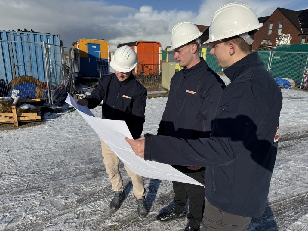 Drie vakmensen van Bouwsector Nederland met witte helm bekijken een bouwtekening op een bouwplaats