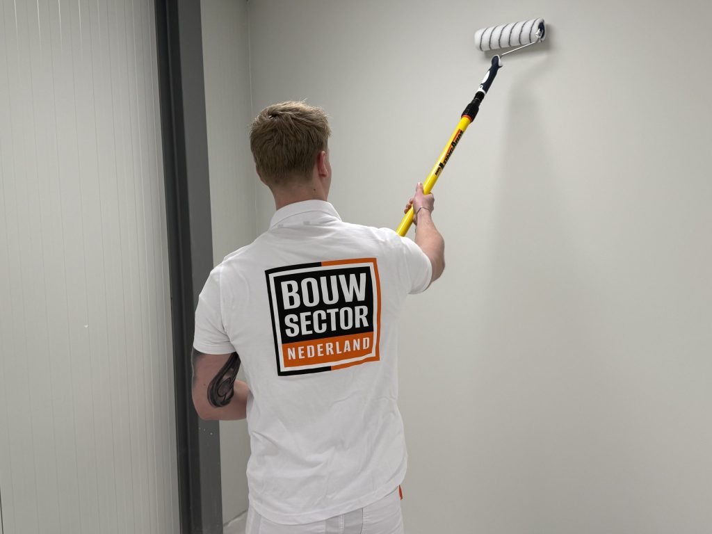 Schilder van Bouwsector Nederland, op de rug gezien, rolt een lichte wand tot bovenin met een roller op een gele steel